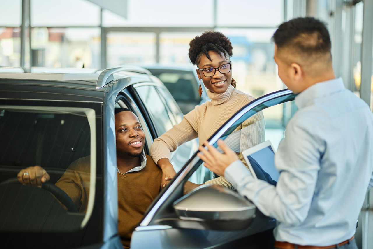 Happy African American couple communicating with car salesperson while buying a car in a showroom.