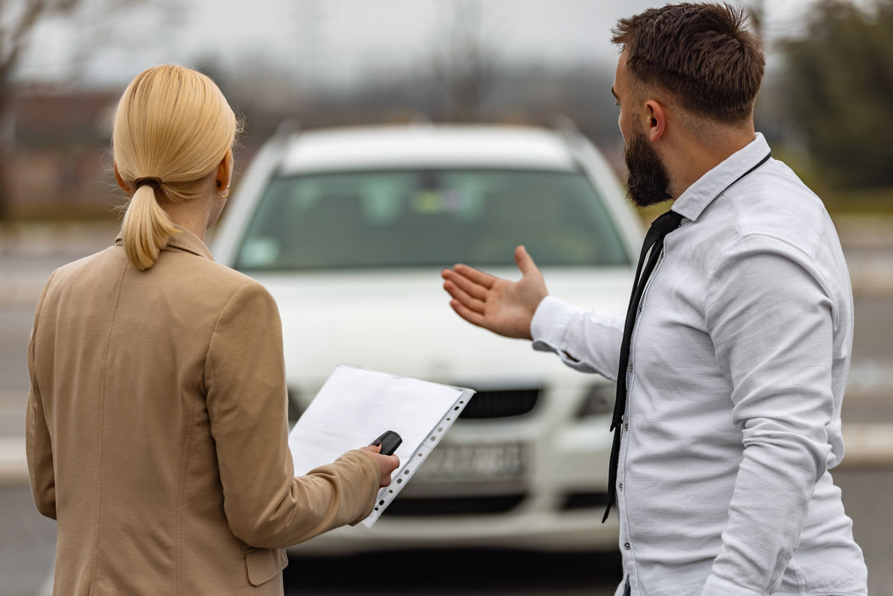 Young man and woman in a car rental service standing while looking at car.