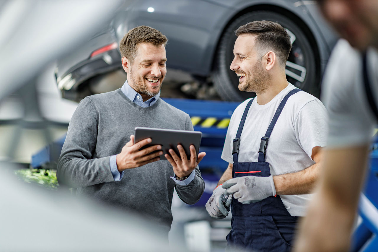 Happy manager and auto mechanic cooperating while using digital tablet in a repair shop.
