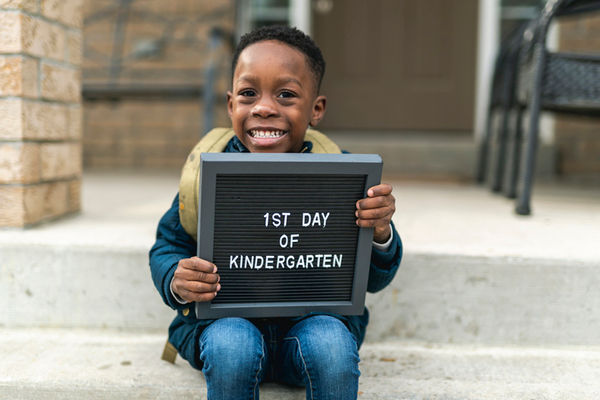 A boy sits on a step with a "1st day of kindergarten" sign