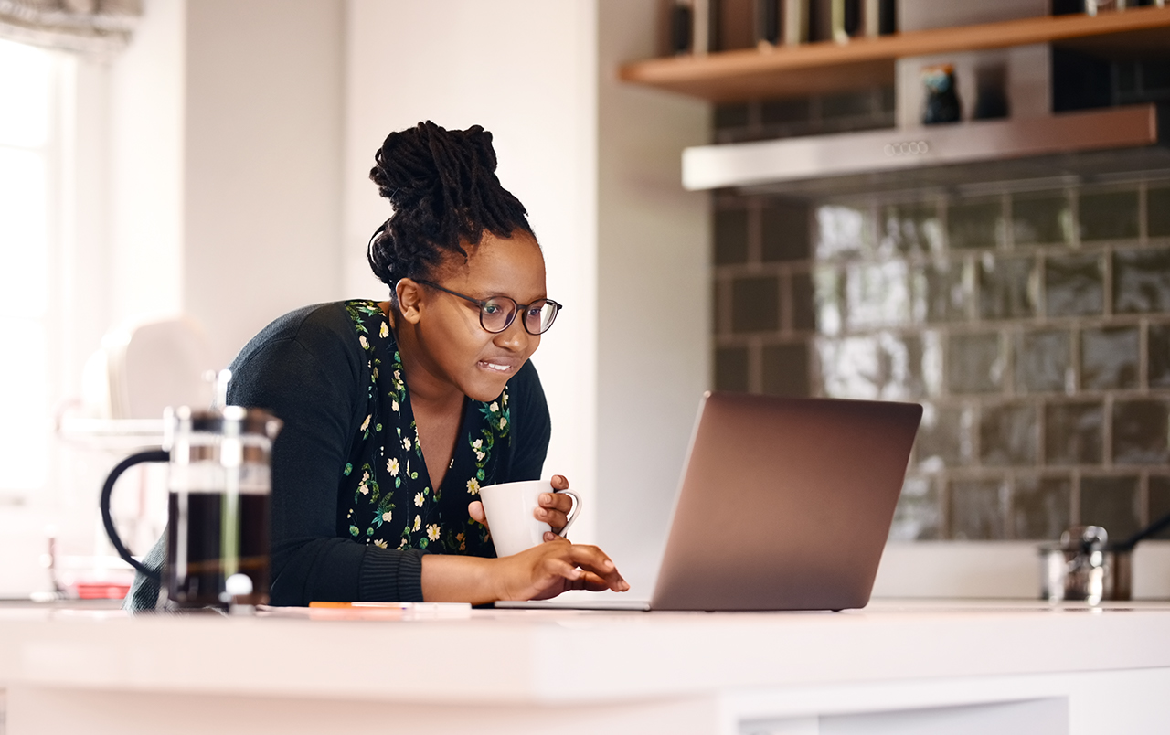 Shot of a young african american woman with a coffee cup using laptop in kitchen at home