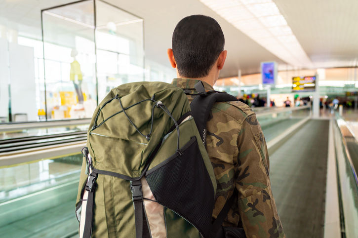 Rearview shot of an unrecognizable soldier in a military uniform standing on a moving walkway in the airport