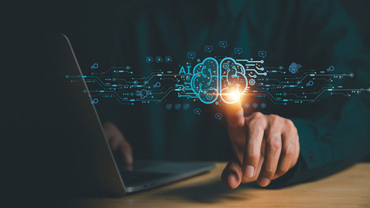 Man at laptop with finger on glowing holographic image of brain and letters AI