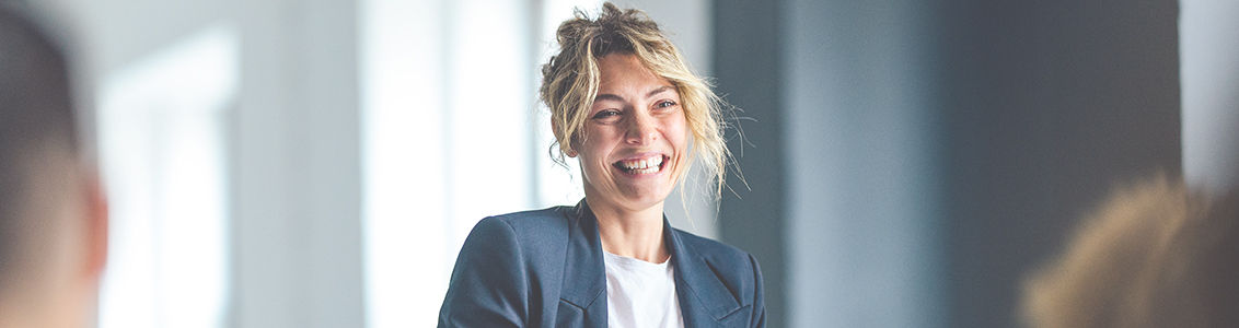 Beautiful cheerful woman in a dark blue jacket standing in front of a crowd looking down at a tablet.