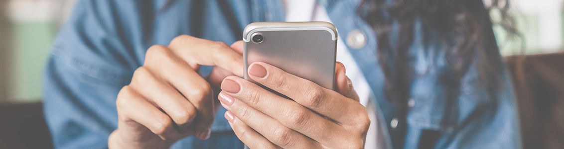 Cropped shot of an african-american young woman using smart phone at home.Smiling african american woman using smartphone at home, messaging or browsing social networks while relaxing on couch