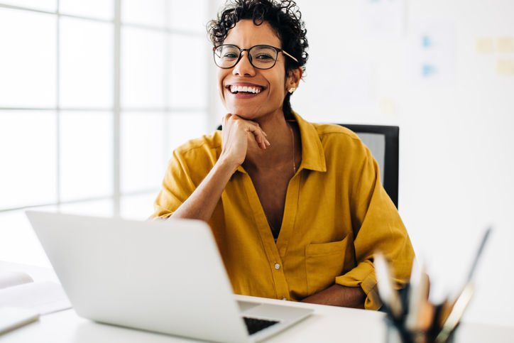 Professional business woman smiling at the camera. Woman sitting at her office desk in business casual. Female professional working in a tech company.