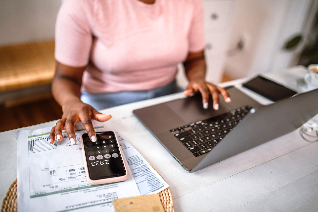 Woman managing home finances using smart phone calculator app and laptop