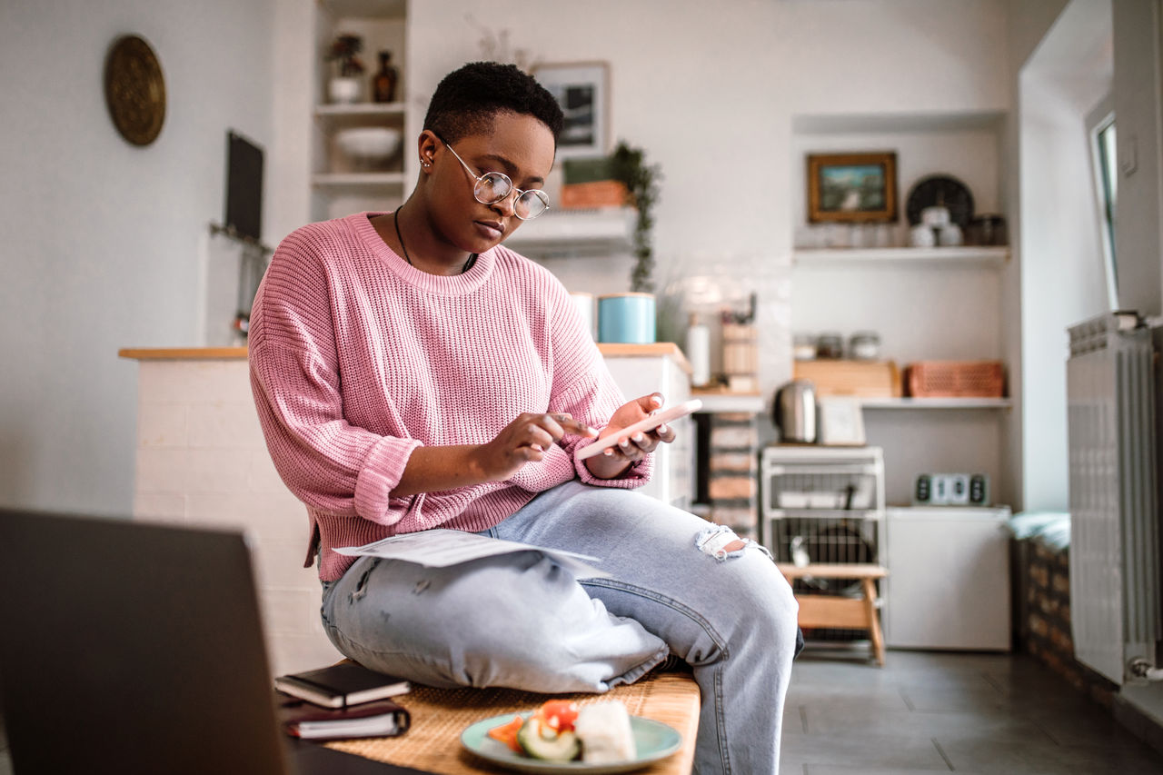 Young woman doing home finances at home in the morning, while having a breakfast