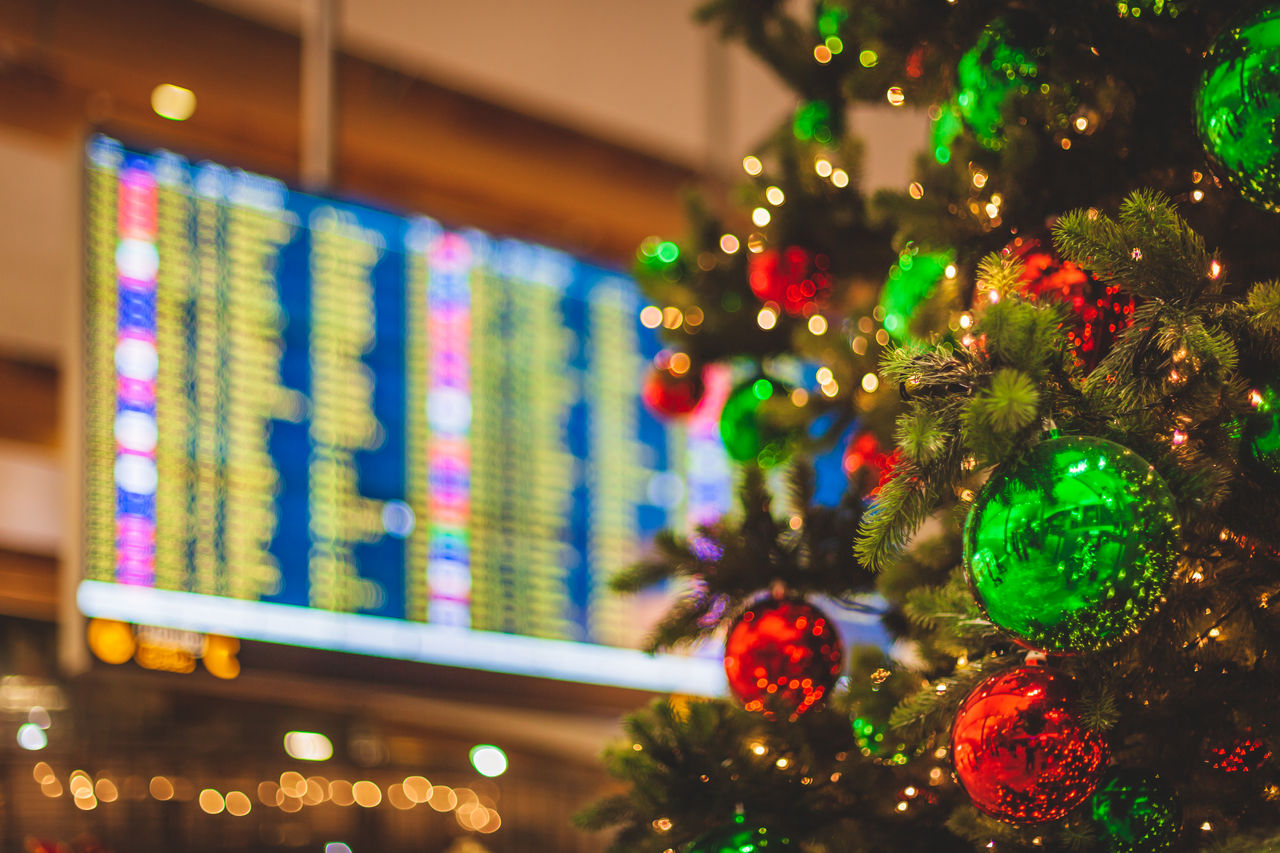 An unrecognizable airport location with a decorated Christmas Tree in the foreground an a flight departures display visible in the background