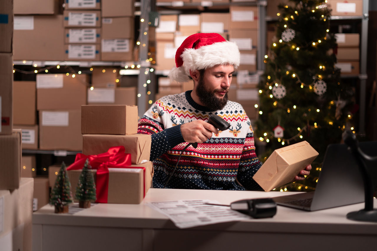 Santa scanning barcode on delivery parcel. Worker scan barcode of cardboard packages before delivery at storage working on Christmas. Male manager factory warehouse scanning labels on the boxes