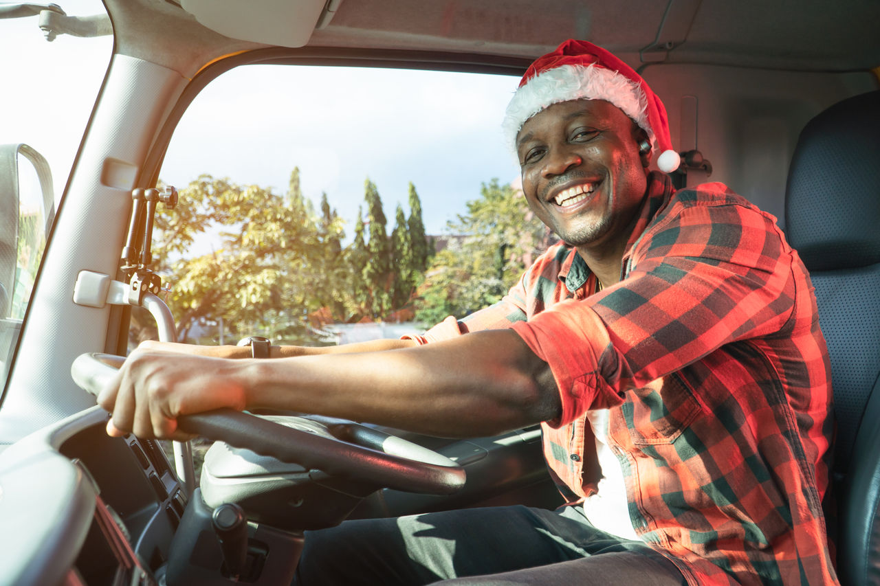 Smile Confidence truck driver wear Santa Clause hat driving semi-truck In Business Long transport. Trucker lifestyle young man African American working holidays.  Merry Christmas and happy new year.