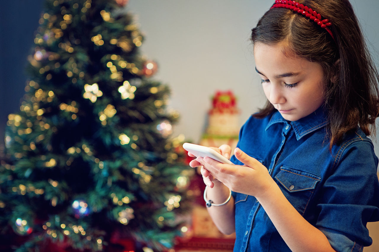 Little girl is texting at the front of Christmas tree