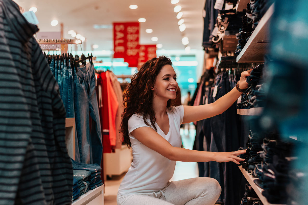 Smiling woman choosing jeans at fashionable shop.