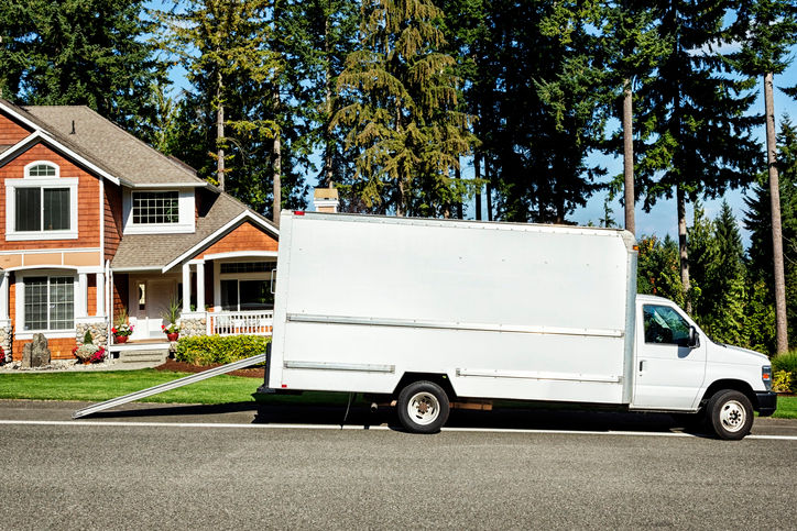 Photo of a plain white moving truck parked on the street in front of a house.