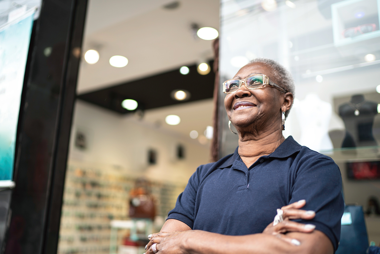 Senior woman standing in front of a store looking away happily with arms crossed