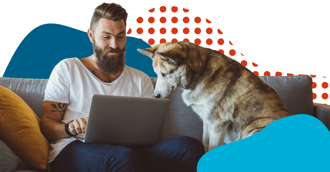 white male sitting on couch with dog looking at computer
