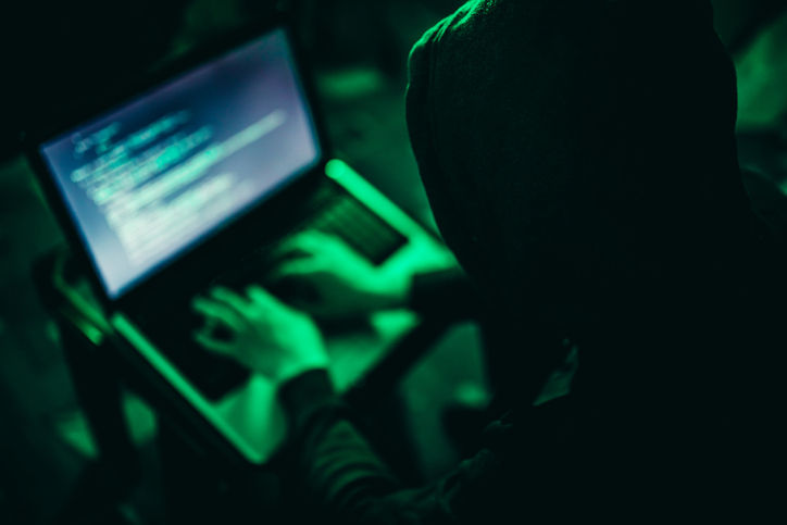 Hacker working on computer at night under green light.