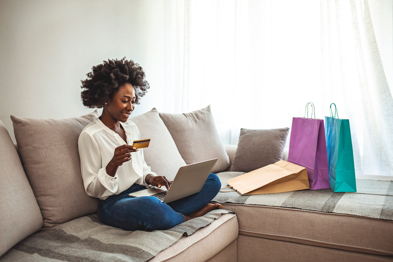 Shot of a young woman using her credit card to make an online payment at home. Wireless retail therapy. Cropped shot of an attractive young woman sitting on her sofa at home and using her tablet for online shopping