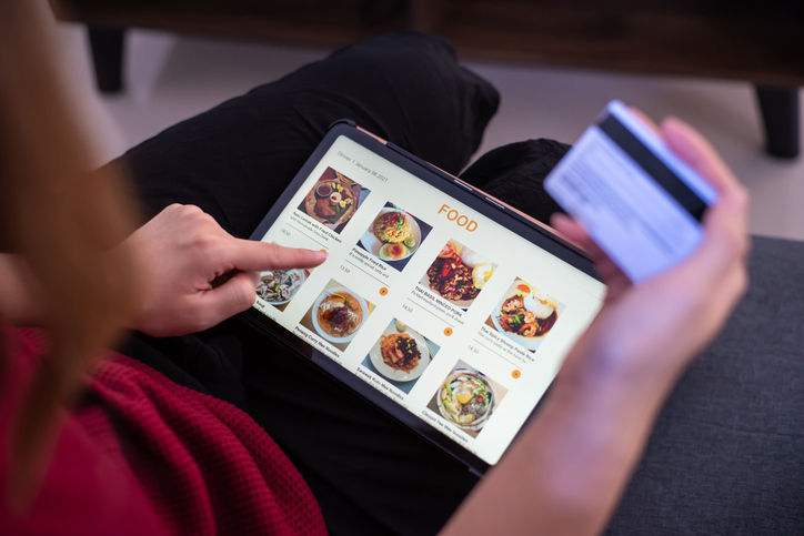 Close-up of a woman holding credit card and digital tablet in hands with online food delivery app showing on screen. The food delivery app showing online food menu with variation of food for selection.