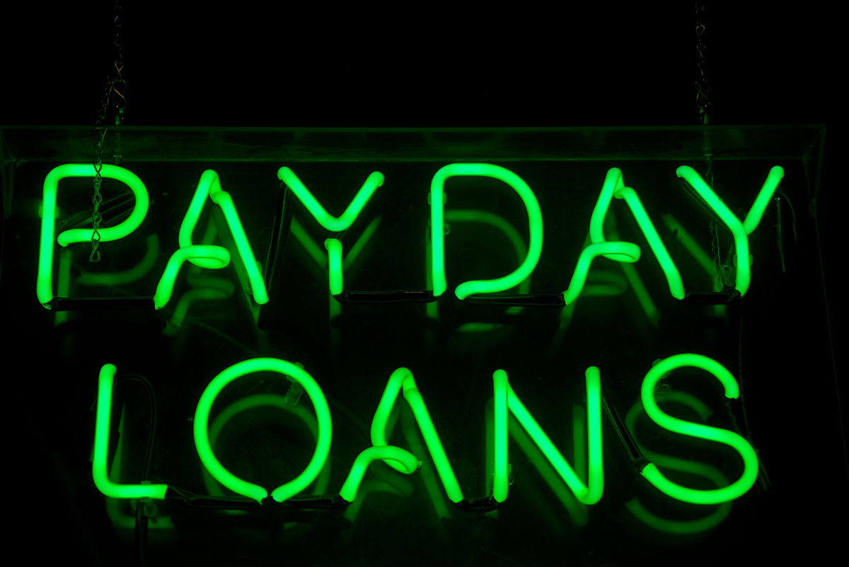 Payday Loans sign glows in green neon message on a black background