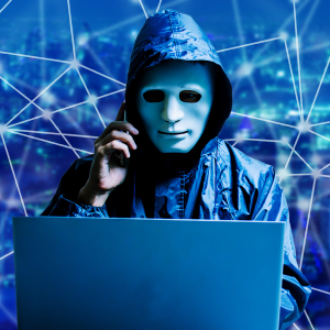 Man with mask sitting behind laptop holding a cell phone to ear