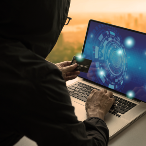 Man in black hoodie with hood up with credit card and laptop open