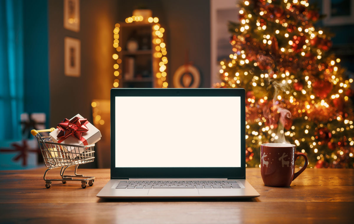 Christmas shopping online at home, laptop with blank screen and miniature shopping cart with a gift inside, holidays and sale concept