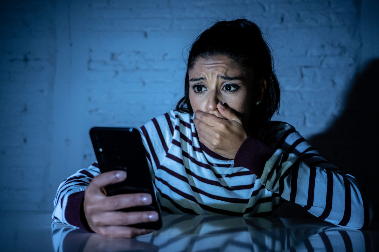 Frightened teenager or young woman using smart mobile cell phone as internet cyberbullying by message stalked abused victim.