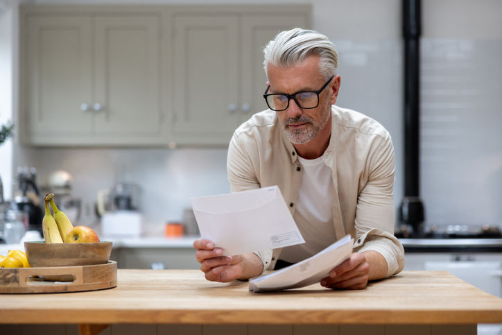 Man at home reading a letter he got in his mail at the kitchen - lifestyle concepts
