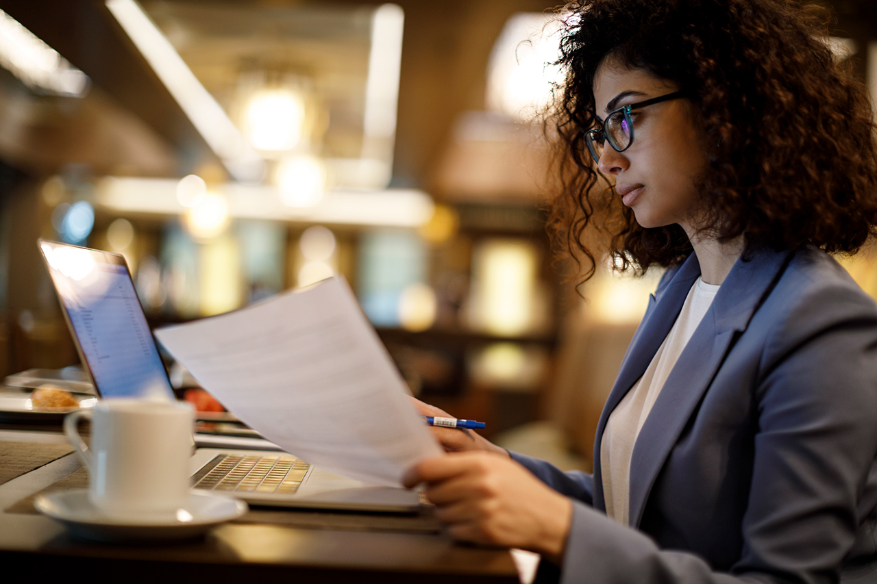 Business woman holding a document and looking at a laptop