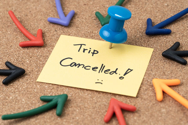 Thumbtack pushpin with multi arrows pointing to small paper note written the words Trip Cancelled.
