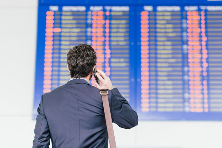 Man looking at the airline schedule and talking on the phone, rear view