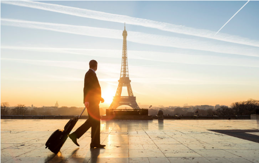man in suit pulling luggage walking by the Eiffel tower