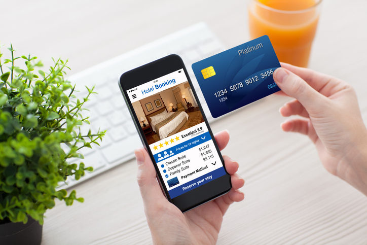 female hands holding phone with app hotel booking screen and credit card in office