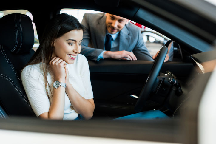 selective focus of smiling girl sitting in car near bearded man in car showroom