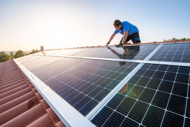 kneeling professional fixing solar panels from the top of a house roof, side view of the roof with sun reflection