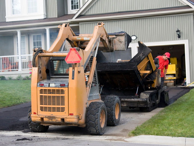 Construction workers loading paving machine with asphalt and paving driveway