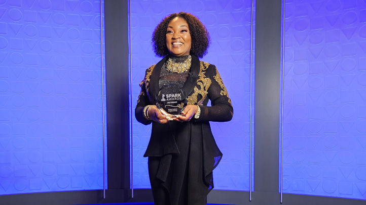 Owner of businesses standing and smiling in front of blue background holding Spark Award