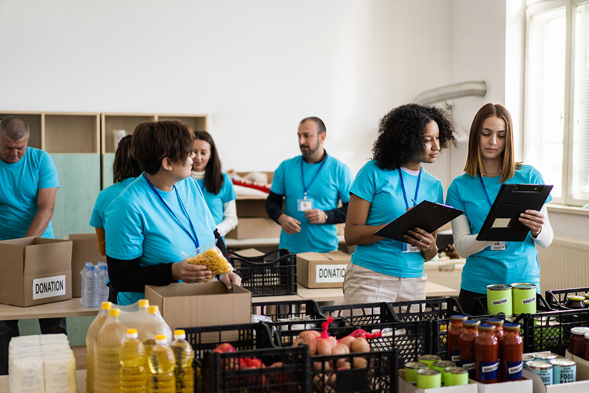 A diverse set of volunteers, wearing matching t-shirts are collecting and counting food supplies for distribution