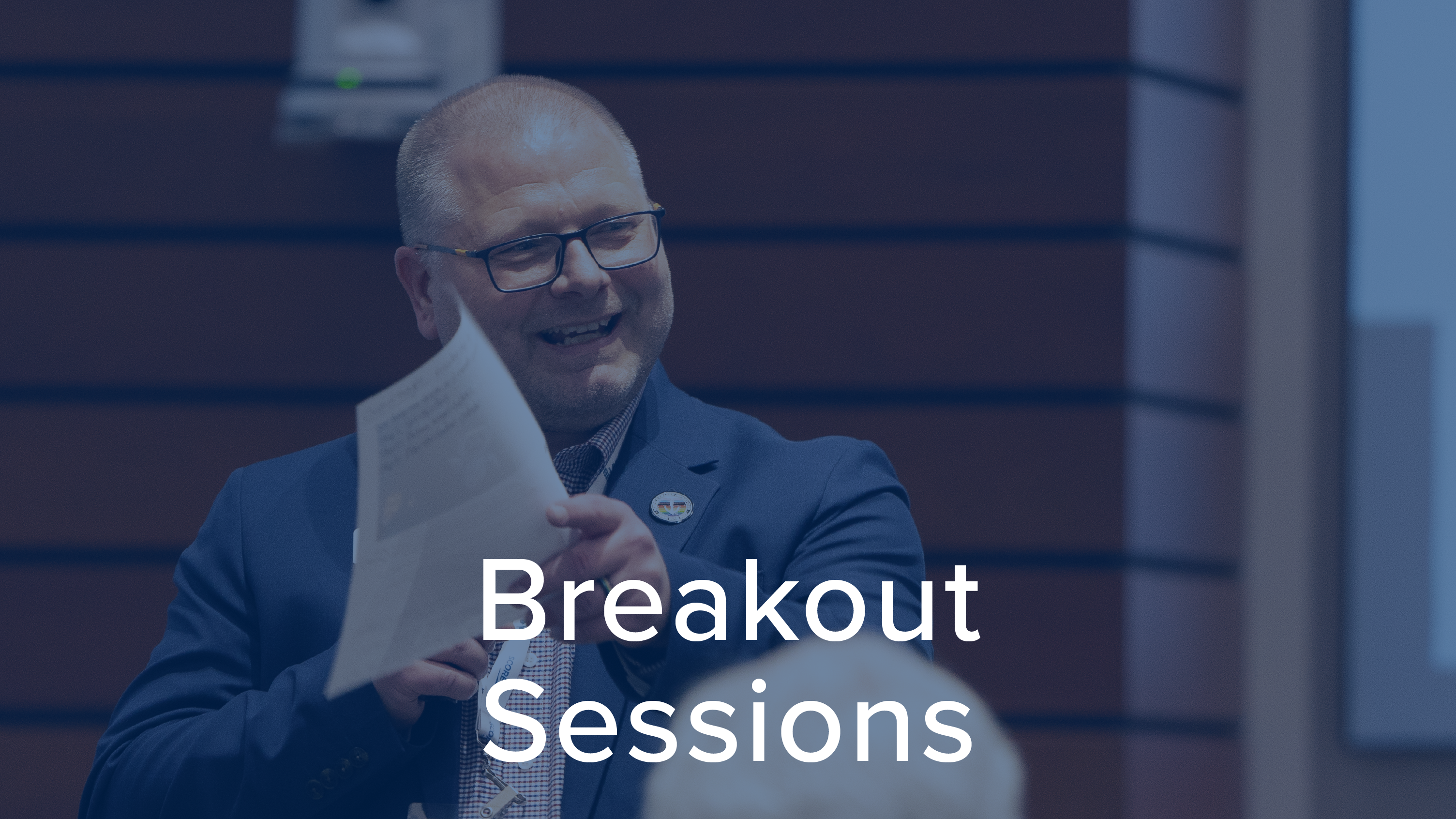 Man wearing glasses, smiling and pointing a handful of papers 