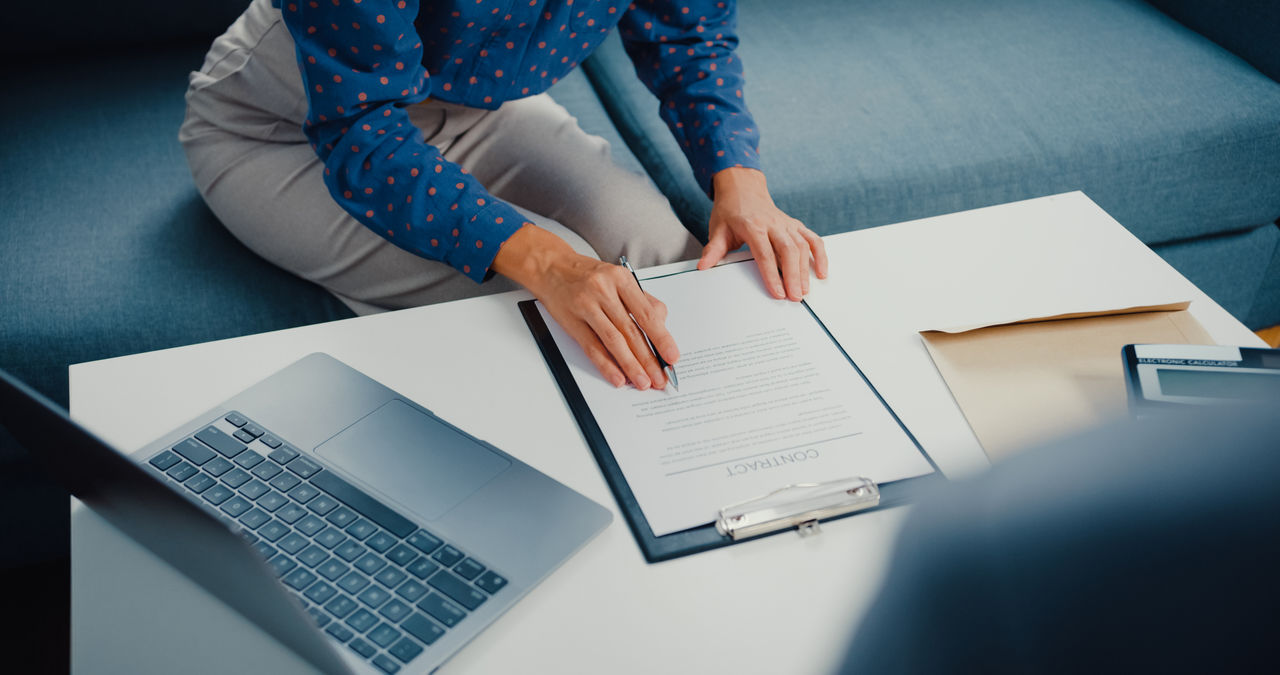 Close up of businesswoman signing mortgage investment contract on sofa in living room at home.
