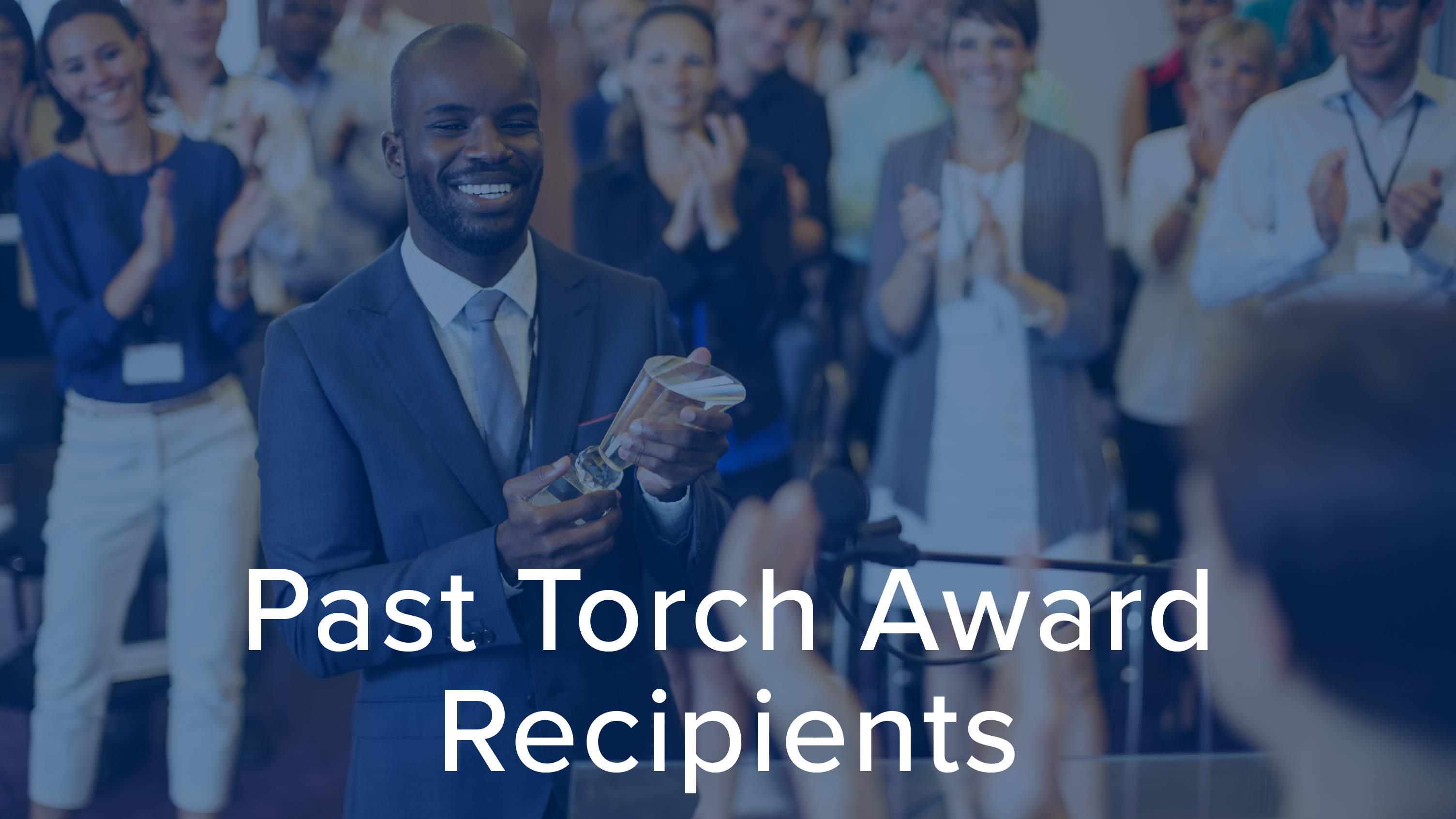 Man smiling holding an award with people clapping all around him