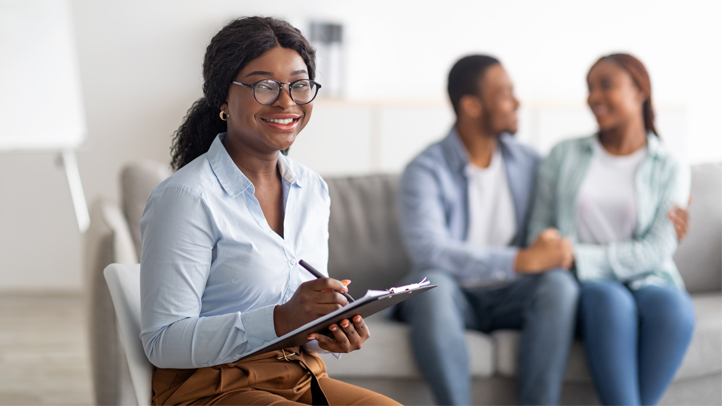 Happy African American psychologist and hugging married couple at office after successful therapy, copy space