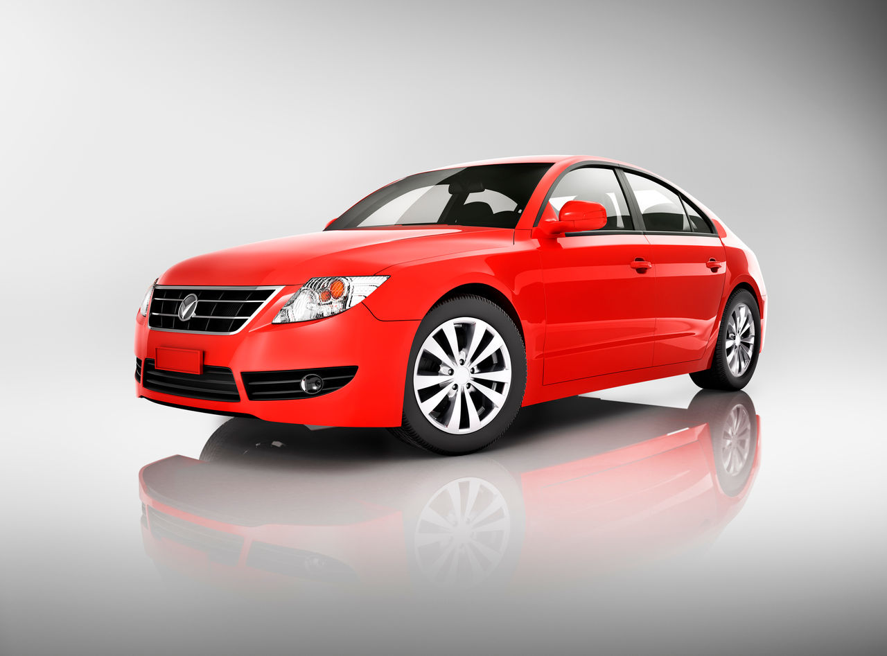 A bright red car set against a shiny gray background.  The car has four doors and is reflected into the glossy surface in the foreground.