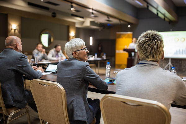 A large group of business conference participants listening to a young woman's speech in a luxury hotel's conference room