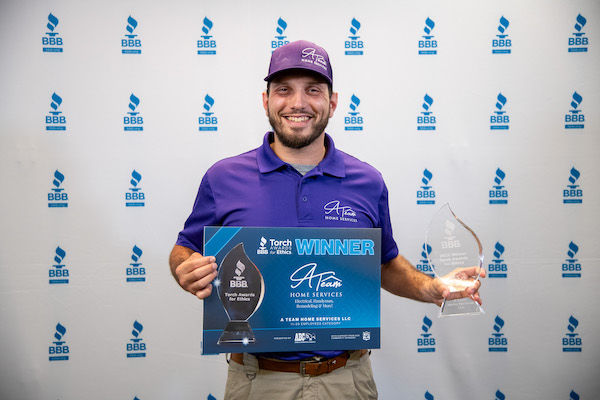 Man holding Torch Award trophy and yard sign