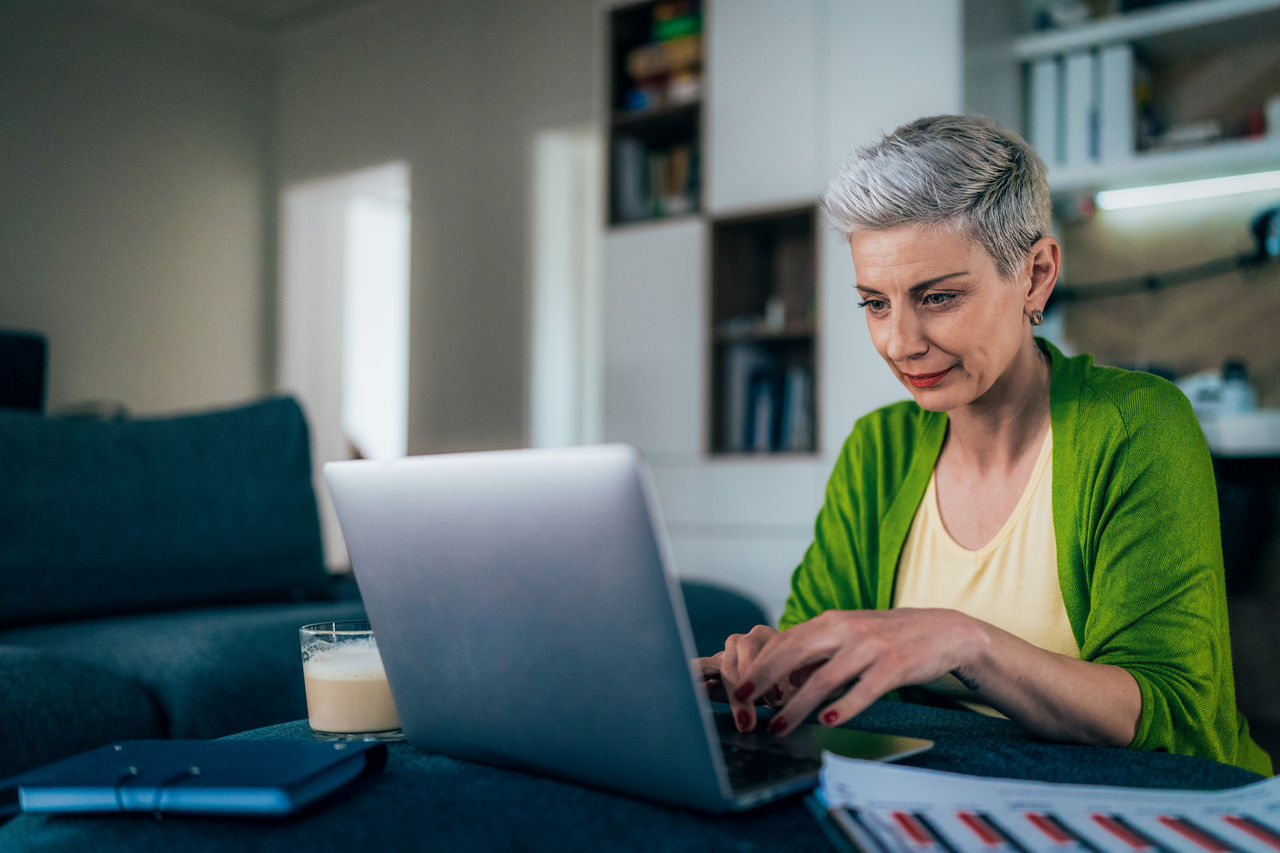 Modern woman working at home. Businesswoman using laptop and documents, drinking coffee. Looking concentrated