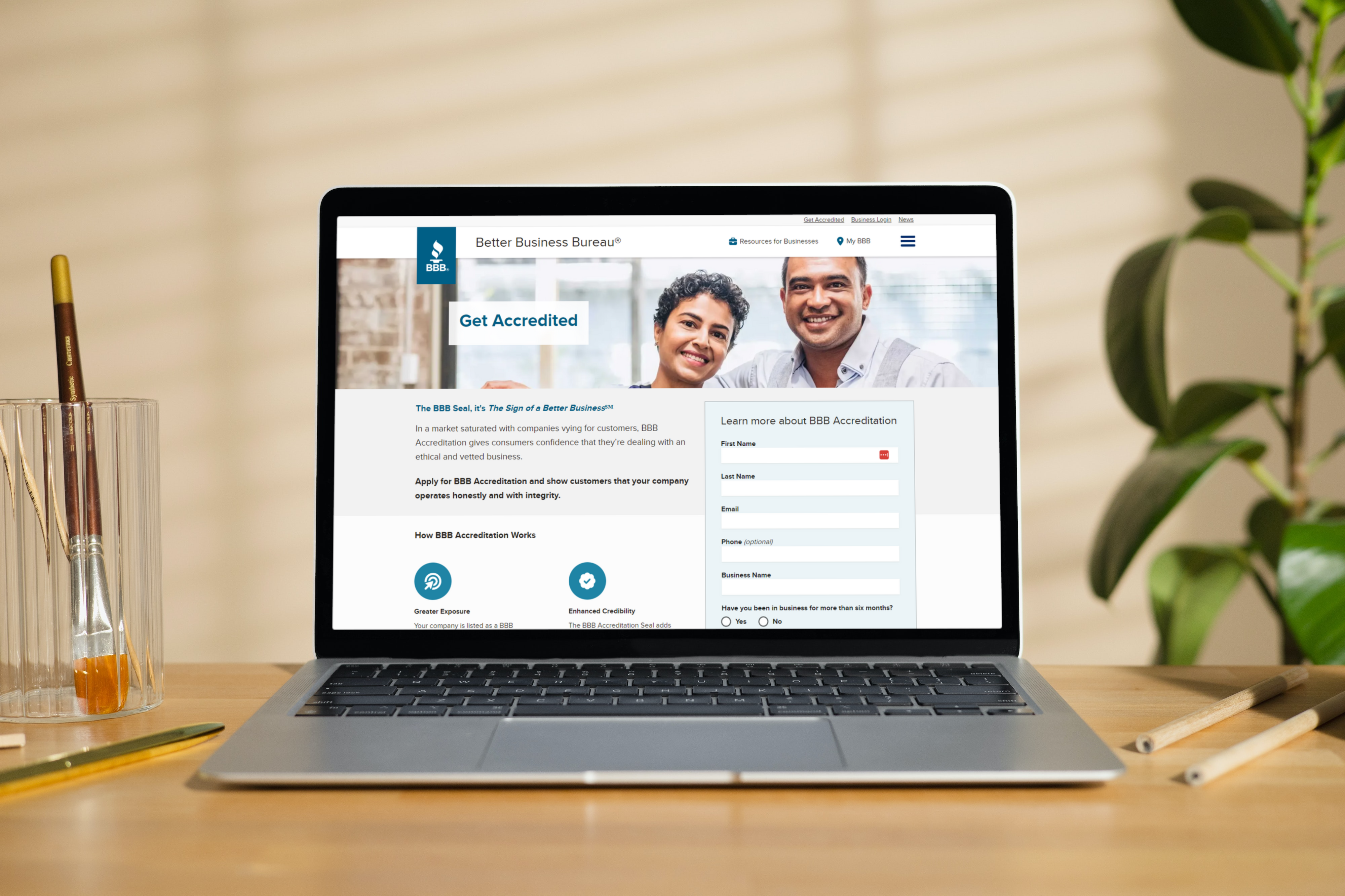 MacBook Air on a wooden desk showing BBB Accreditation page