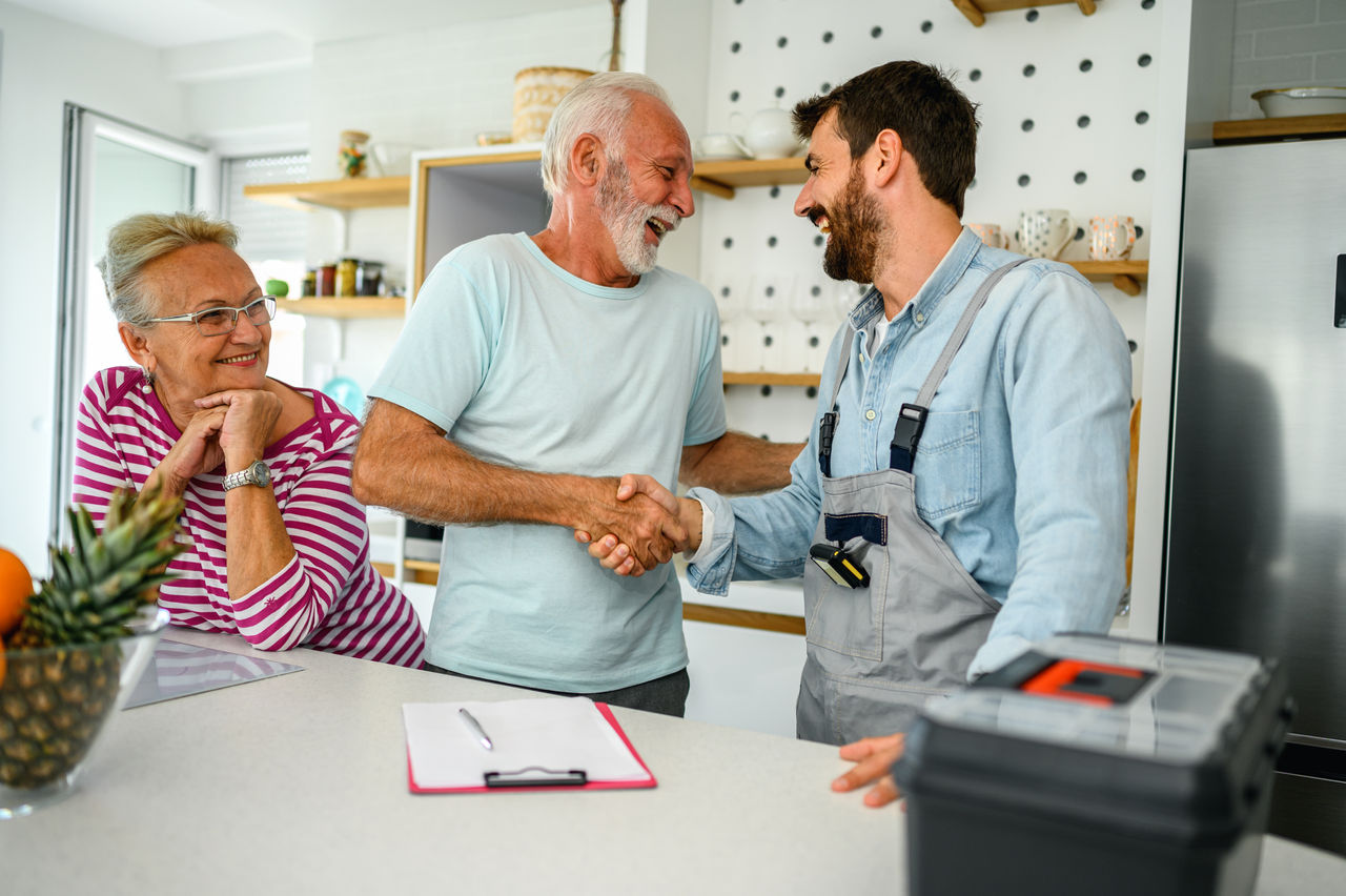 Repairman gives repair estimate to a senior couple. Service Industry: Repairman works at customer's home.