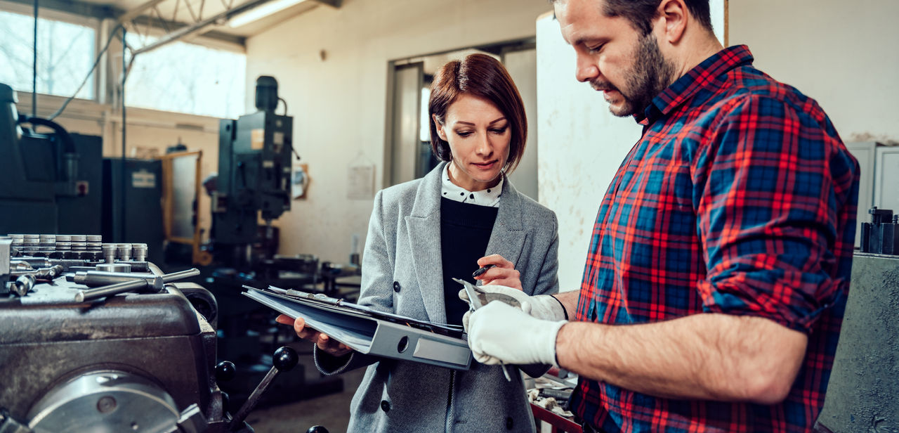 Female engineer consulting with lathe machine operator at industrial manufacturing factory